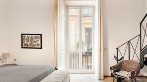 A bedroom with a bed, a chair, a framed picture, and a staircase. - Green Chiaia three (Napoli)