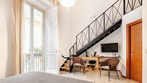 A bedroom with a bed, a desk with two chairs, a TV, and a staircase. - Green Chiaia three (Napoli)