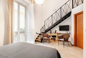 Une chambre à coucher avec un lit, un bureau avec deux chaises, une télévision et un escalier.