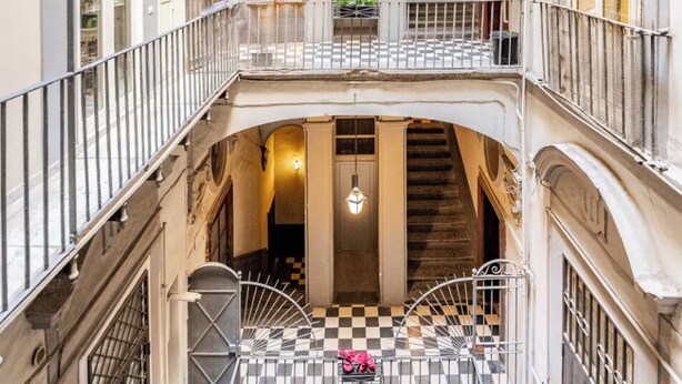 A multi-level interior with balconies, staircases, and a checkered floor. - Green Chiaia three (Napoli)
