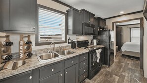 Cocina compacta con armarios oscuros, un lavamanos de acero inoxidable y un microondas.