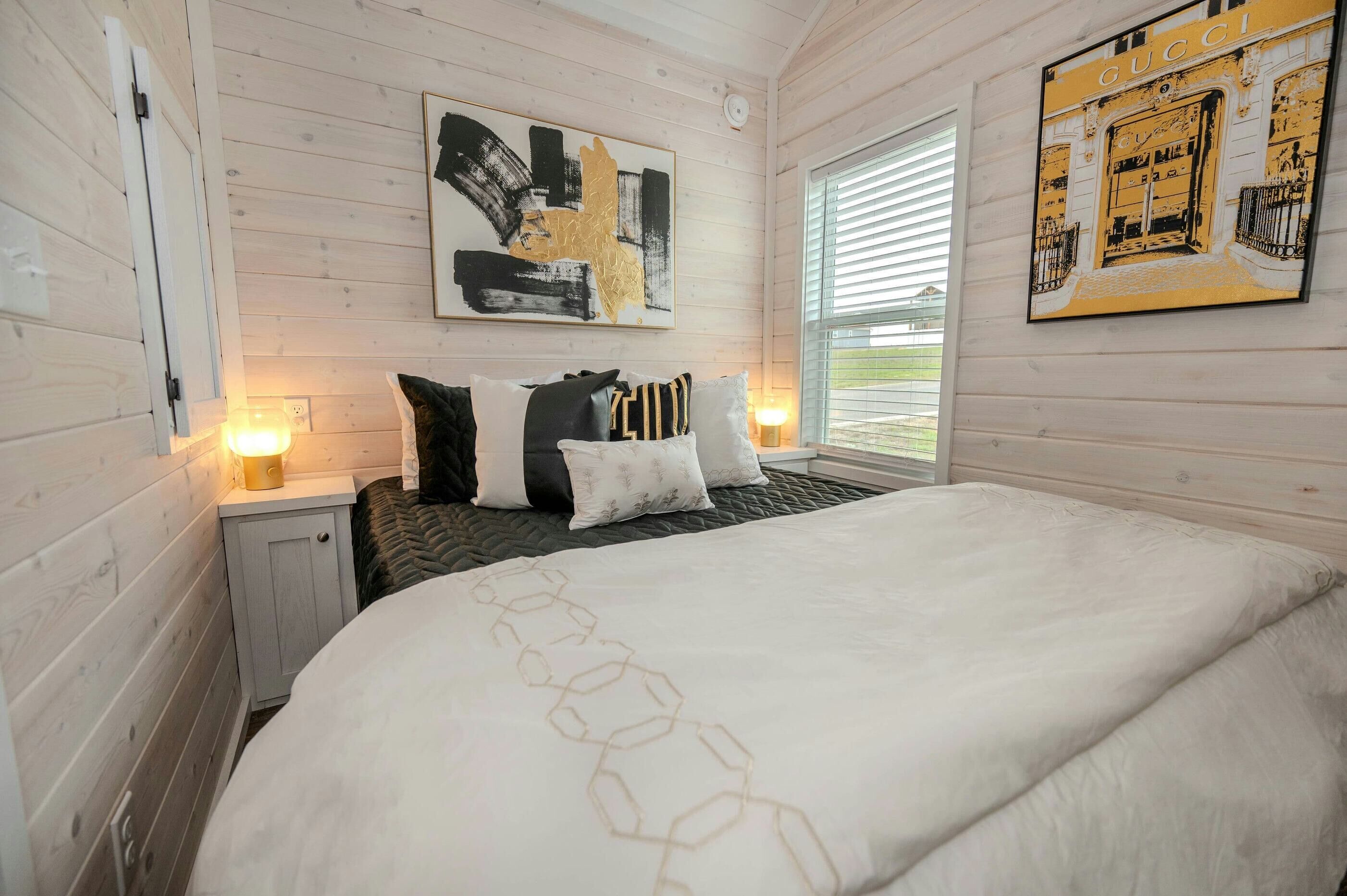 A bedroom with a bed, bedside tables, a window, and artwork on the walls.