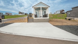 Ein eingeschossiges Haus mit Veranda, Auffahrt und einem grasbewachsenen Hügel im Hintergrund.