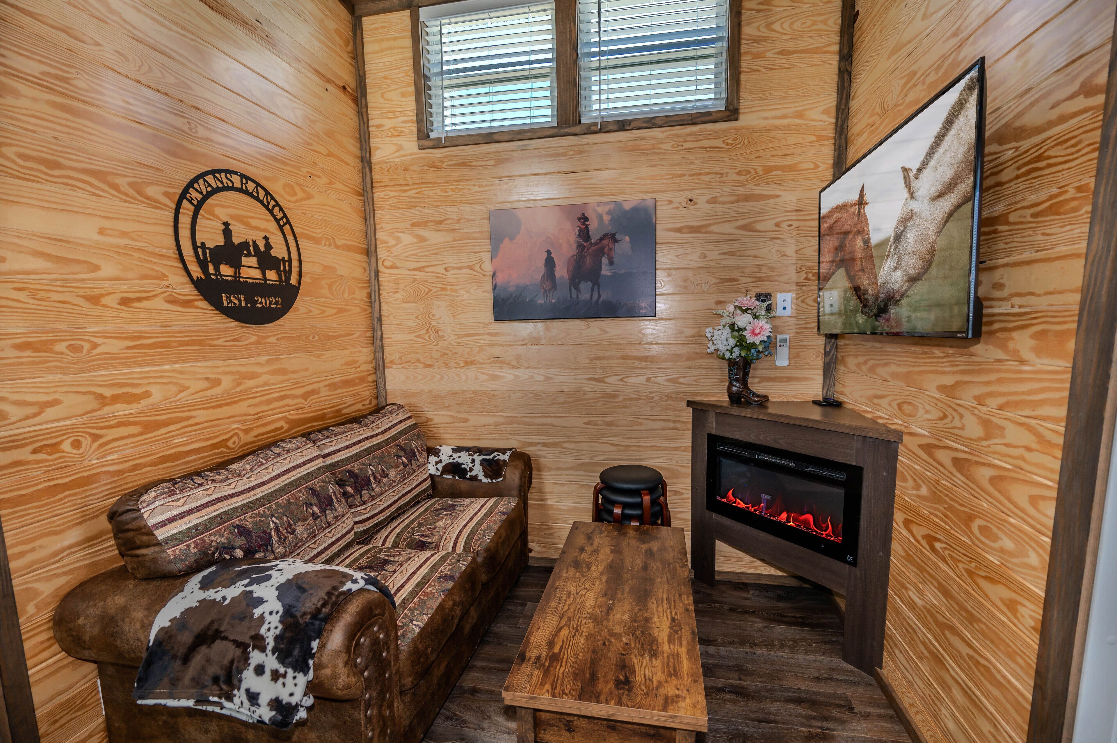 A wooden interior with a sofa, a coffee table, a fireplace, and a mounted picture of horses.