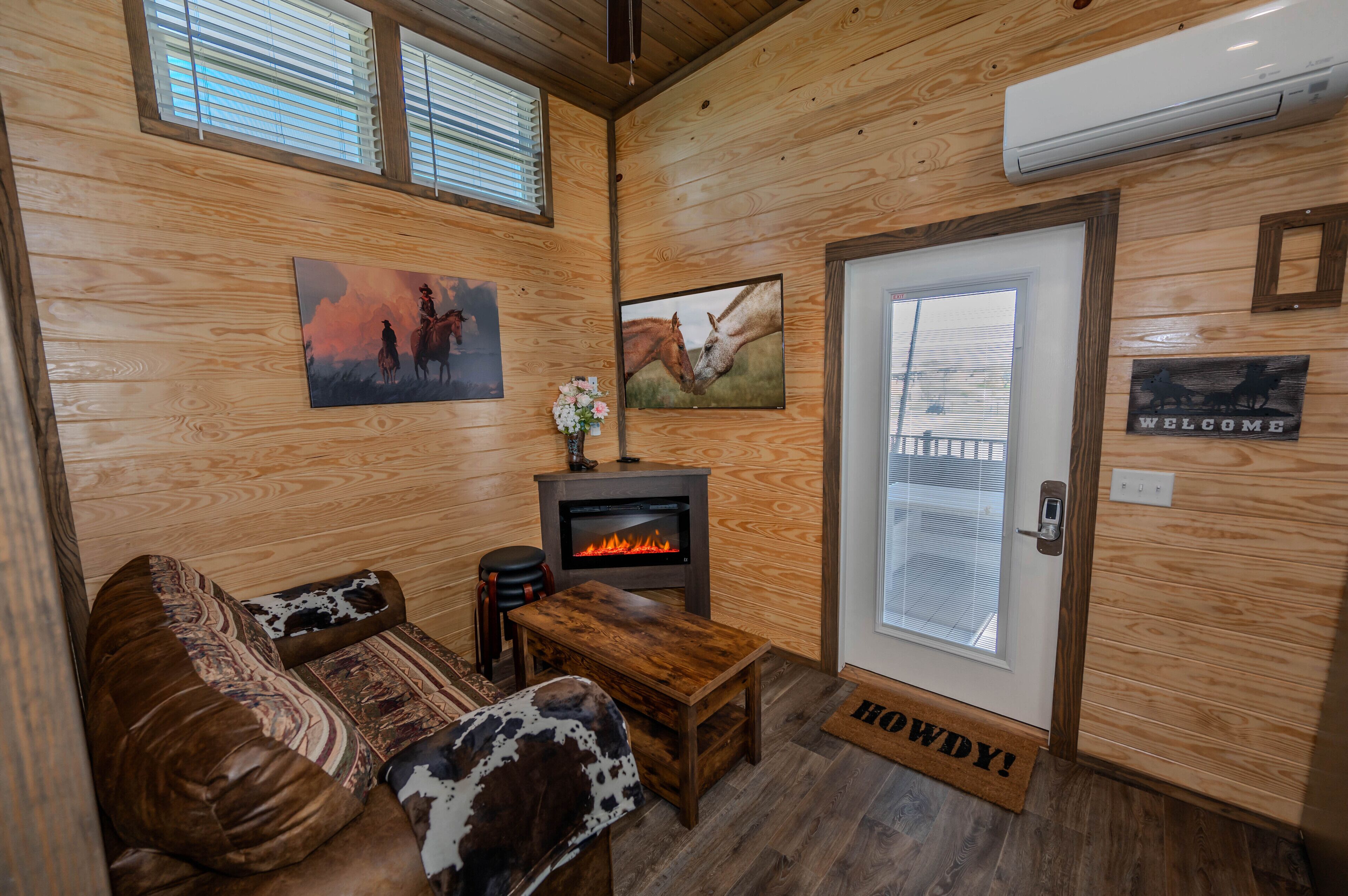 A cozy room with wooden walls, a fireplace, a couch with cowhide cushions, and a welcome sign.