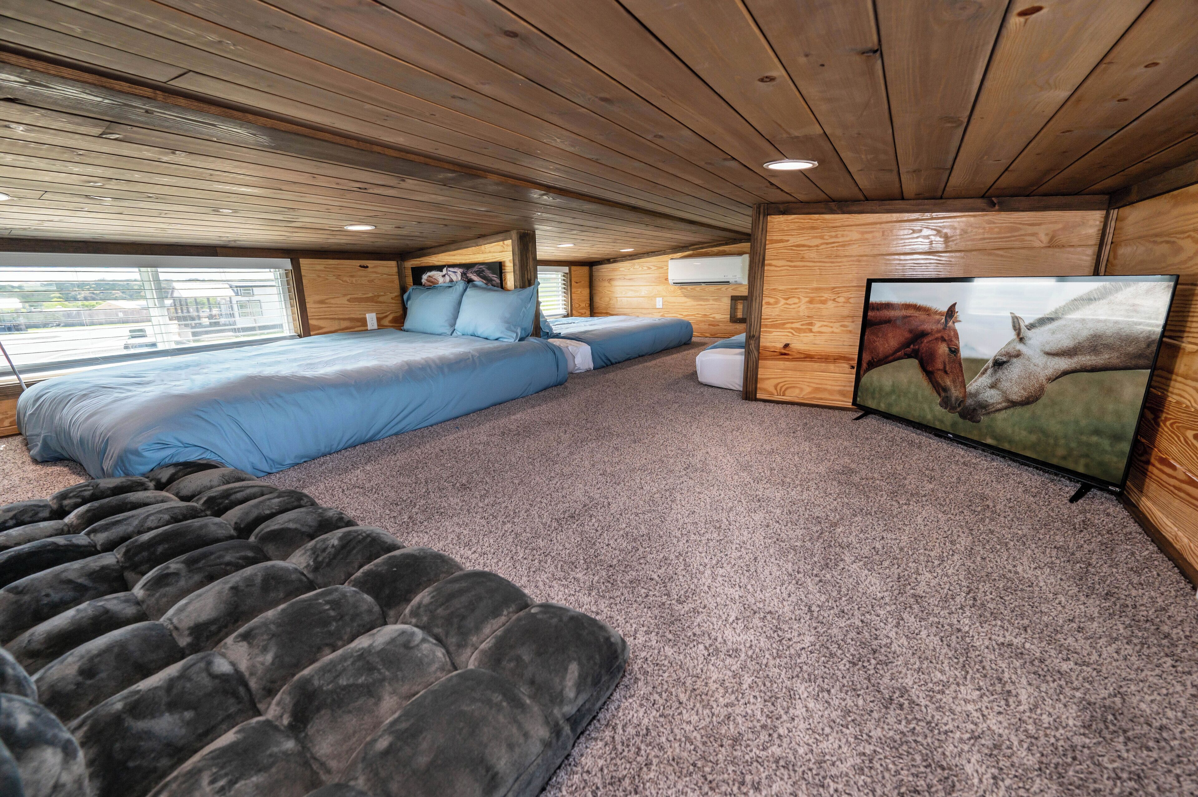 A bedroom with a large bed, a smaller bed, a sofa, and a TV displaying horses.
