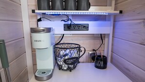 A kitchenette with a Keurig coffee maker, a coffee basket, and a mug labeled "SUGAR" on a wooden countertop.