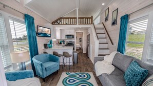 A compact, modern interior with a kitchen, dining area, and living room, featuring a staircase to an upper level.