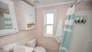 A bathroom with a wooden wall, a white toilet, a sink with a mirror, and a shower curtain.