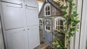 A narrow hallway with a wooden door and a small house model with windows and a wreath. - The Little Haus - 153 (Fredericksburg)