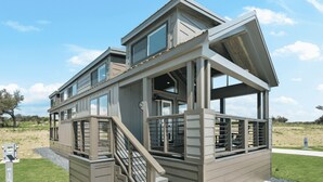 A modern two-story house with a covered porch, a staircase, and a large window overlooking a grassy area.
