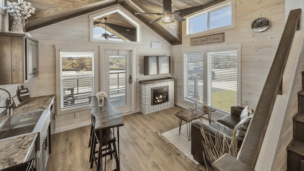 A spacious kitchen with a central island, a fireplace, and a dining area with a high ceiling and wooden beams.
