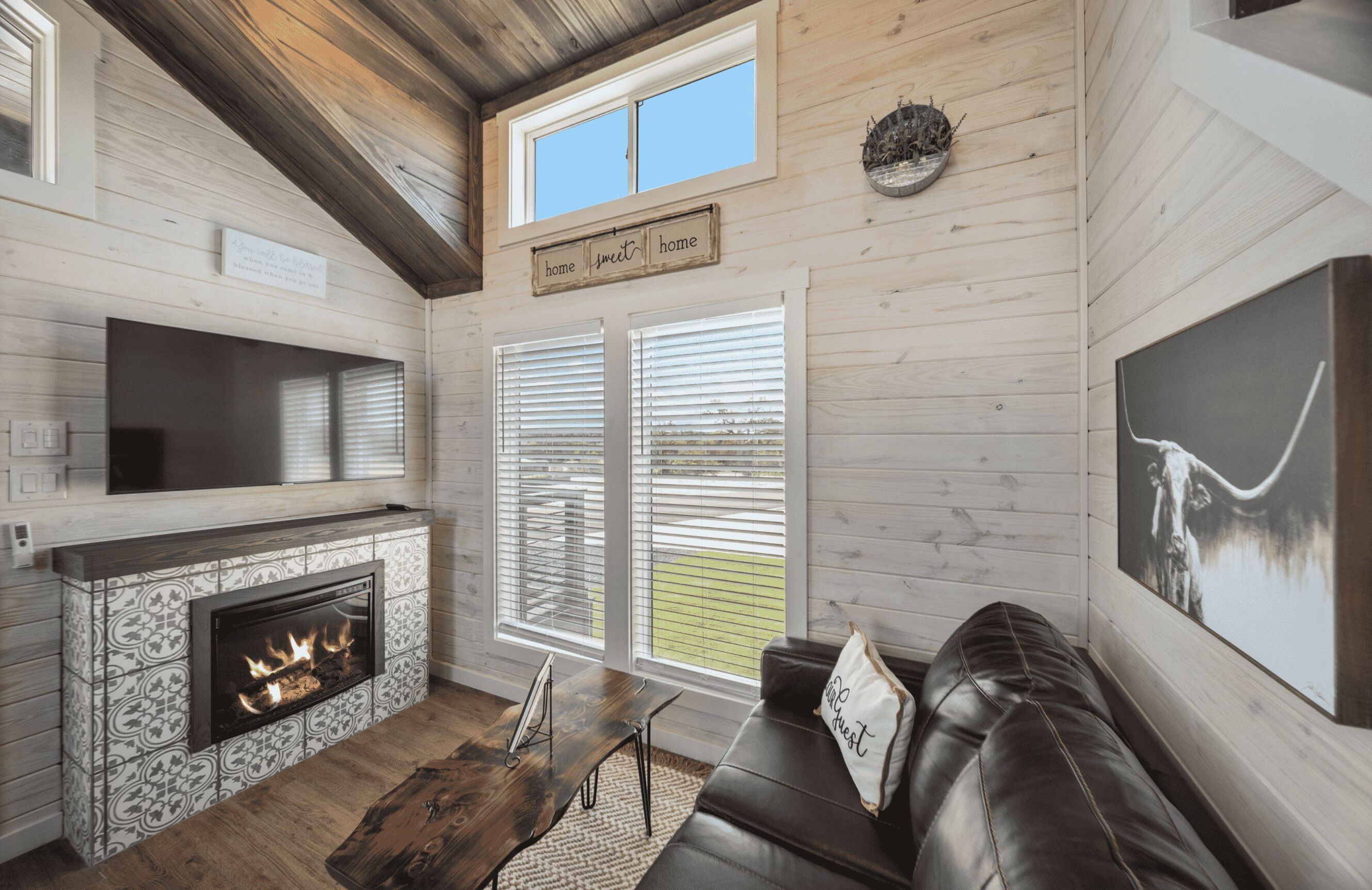 A cozy living room with a fireplace, a leather sofa, and a large window with blinds.