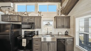A modern kitchen with dark wood cabinets, stainless steel appliances, and a view of the outdoors through large windows.