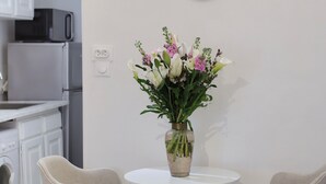A kitchen with white cabinets, a microwave, and a washing machine. There is a round table with a vase of flowers and two chairs. A clock is on the wall. - Beautiful Apartment in the Old Town - Close to the Sea (Nice)