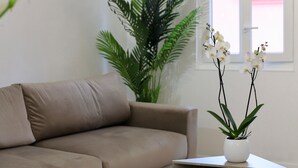 A modern living room with a beige sofa, a white coffee table, and a potted plant with white orchids. - Beautiful Apartment in the Old Town - Close to the Sea (Nice)