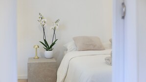 A minimalist bedroom with a bed, a bedside table with a lamp, and a potted plant. - Beautiful Apartment in the Old Town - Close to the Sea (Nice)