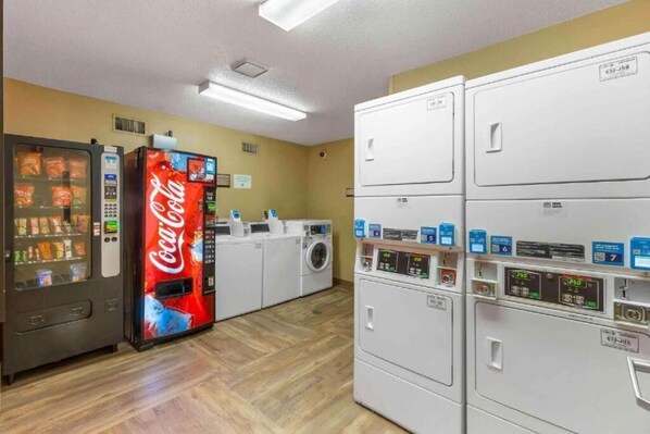 A laundry room with a Coca-Cola vending machine, multiple washing machines, and dryers.