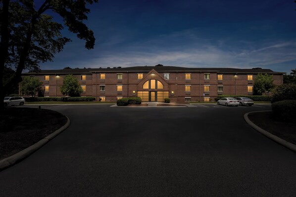 A multi-story brick building with a central entrance, surrounded by a parking area with cars.