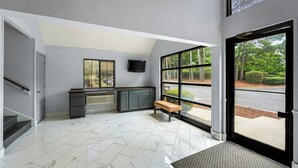 A modern room with a desk, bench, and large windows offering a view of the outdoors. - Deluxe Studio at Extended Stay Cary 2 (Cary)