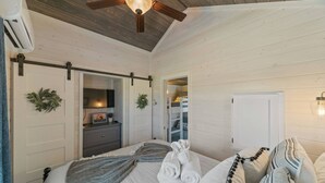 Un dormitorio con cama, ventilador de techo, cómoda y puerta que da a otra habitación.