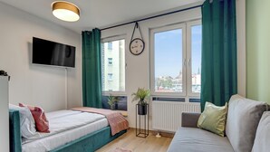 Moderni makuuhuone, jossa on sänky, sohva, televisio, kello ja ikkuna, jossa on verhot.