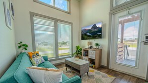 A living room with a teal sofa, a coffee table, and a large window with blinds.
