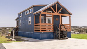 A small, single-story building with a blue exterior and wooden accents, featuring a porch and a staircase leading to the entrance.