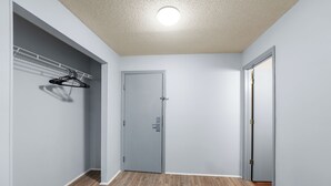 A hallway with a wooden floor, a grey door, and a clothes rack with hangers. - Deluxe Studio at Extended Stay Cary 3 (Cary)