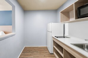 A compact kitchen with a built-in refrigerator, a microwave, and a sink. - Deluxe Studio at Extended Stay Cary 3 (Cary)