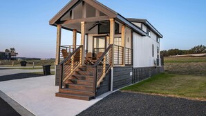 A modern house with a covered porch, wooden stairs, and a small outdoor seating area. - Rinconcito Magico - 200 (Fredericksburg)