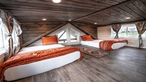 Dormitorio tipo loft con dos camas, vigas de madera en el techo y un ventanal grande.