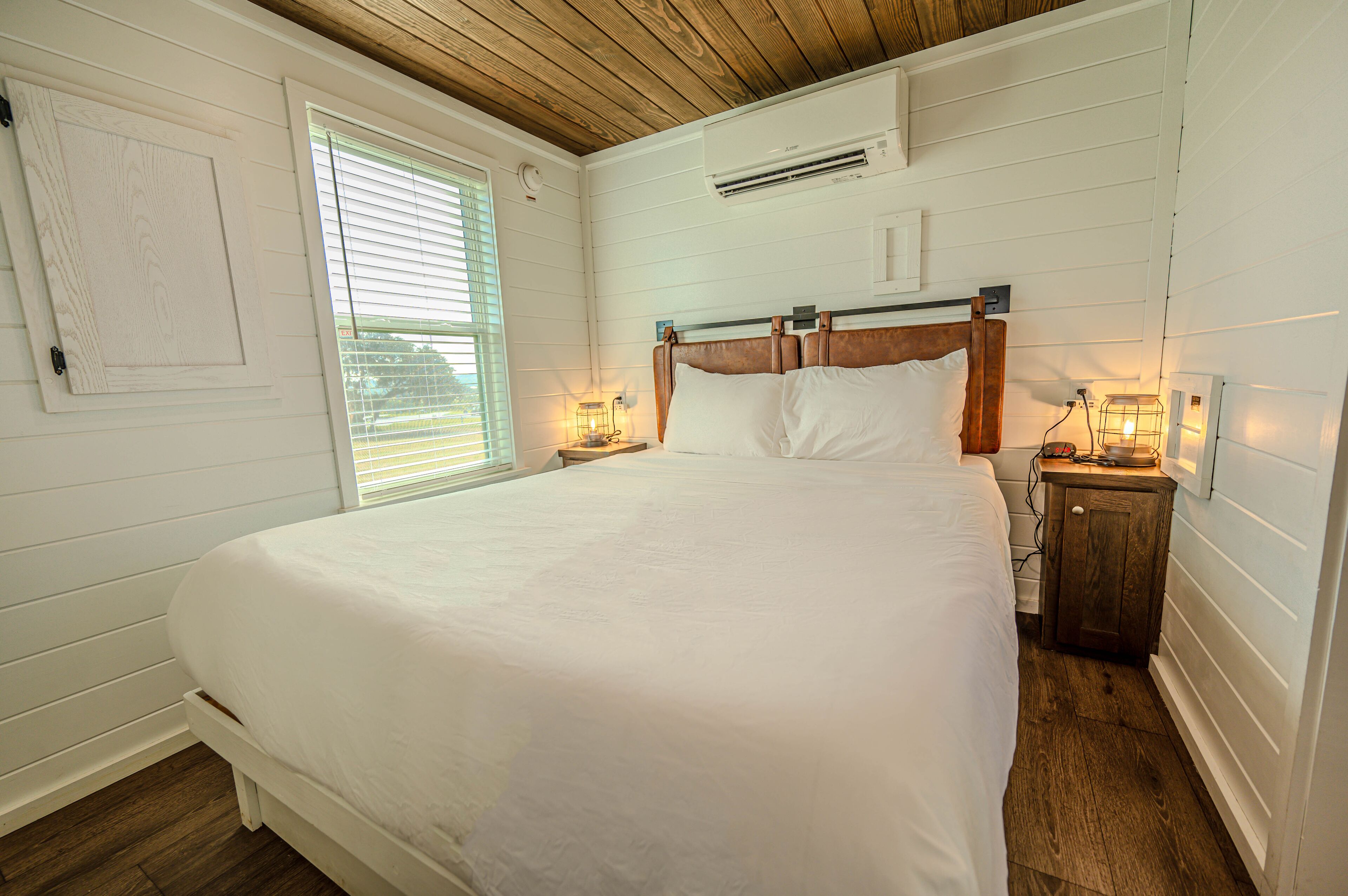 Un dormitorio con una cama grande, cabecera de madera, lámparas de noche, una mesita de noche y una ventana con persianas.