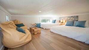 A spacious bedroom with a large bean bag chair, two single beds, a wooden crate, and a window with a view.