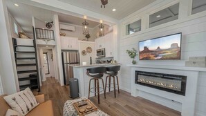 A modern kitchen with white cabinets, a large island, and a flat-screen TV above the fireplace.
