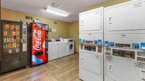 Una lavanderia con una macchina distributrice di Coca-Cola, diverse lavatrici e asciugatrici.