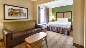 Camera d'albergo con divano in pelle marrone, tavolino in legno, un letto con biancheria bianca, un quadro appeso al muro e una finestra con tende.