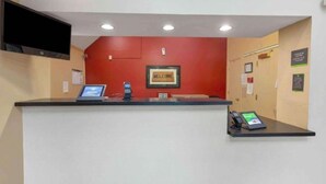 Una reception con una parete rossa, un cartello con la scritta 'WELCOME' e un televisore a parete, oltre a un telefono.