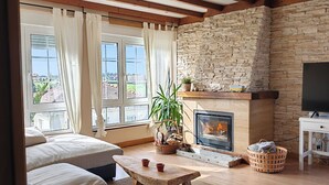 A cozy living room with a fireplace, a stone wall, and a large window with curtains.