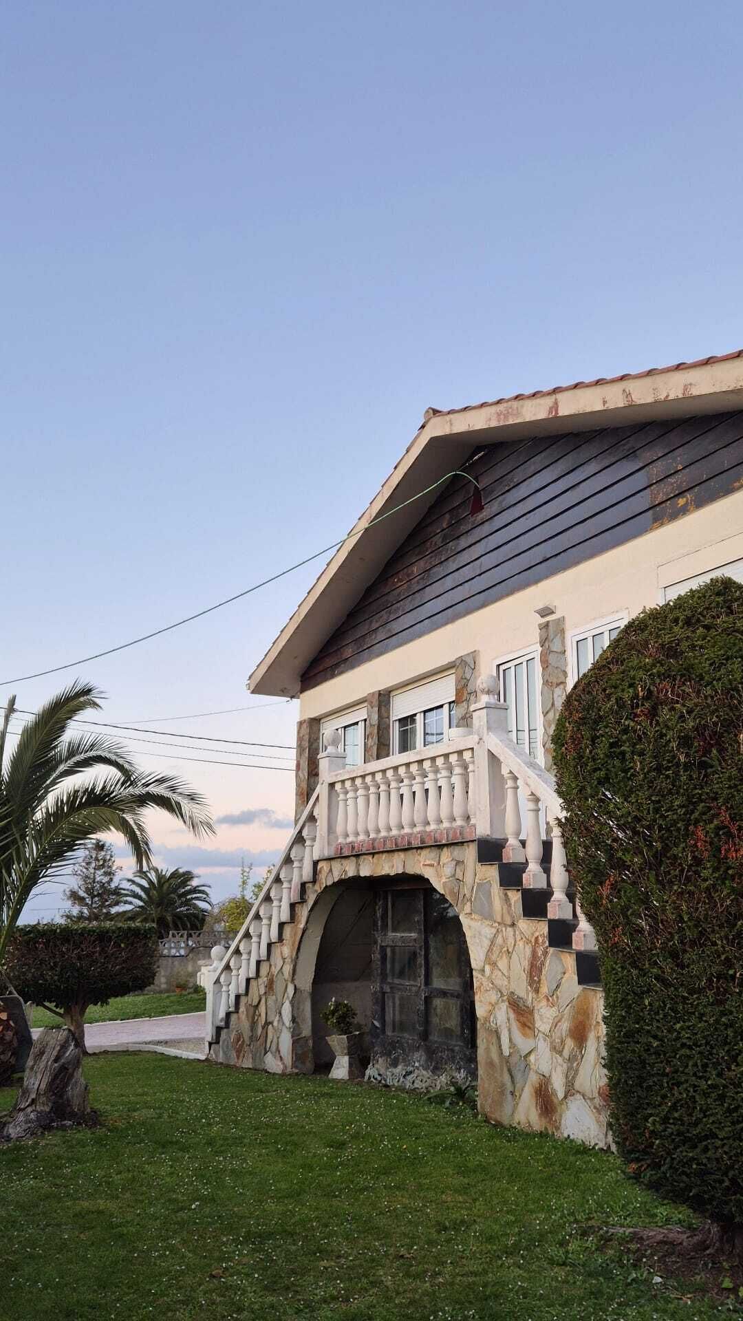 Una casa con un arco de piedra en la entrada, un balcón con barandilla y un césped bien cuidado.