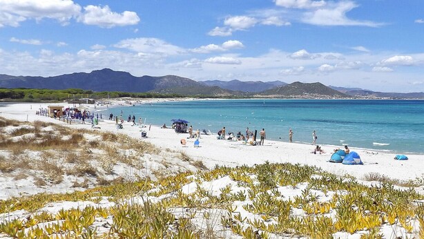 A beach with people sunbathing and swimming, tents set up, and mountains in the background. - Happy Camp in Selema Camping (Siniscola)