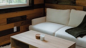 A cozy room with a white sofa, a wooden coffee table, and a window with a view of trees.