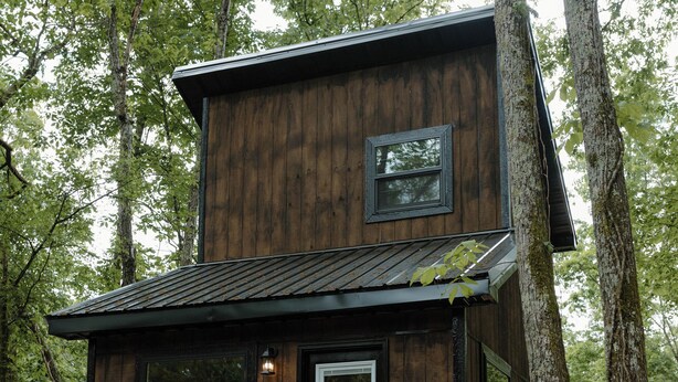 A wooden cabin with a staircase leading to a deck, surrounded by trees.