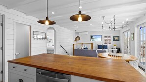 Una cocina con encimera de madera, lavavajillas de acero inoxidable, luces colgantes y un comedor con mesa redonda y sillas.
