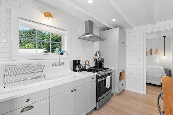 A modern kitchen with white cabinetry, a stainless steel stove, and a window with a view of greenery. - Harborside Cottage, walk to downtown (Rockland)