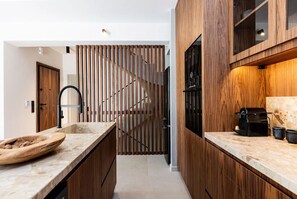 A modern kitchen with wooden cabinets, a marble countertop, and a built-in coffee machine. - Award Winning Villa w BBQ, Sauna & 250m to Beach (Μυρθιανος Πλακιάς)