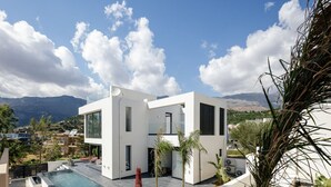 Une maison moderne avec une piscine, une façade blanche et une vue sur les montagnes.