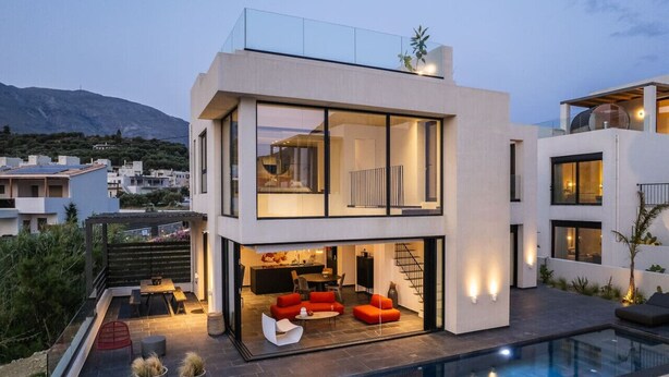 Une maison moderne à deux étages, dotée d’une façade en verre, d’une terrasse sur le toit et d’une piscine.