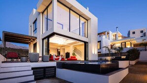 Une maison moderne à deux étages, dotée d’une grande façade vitrée, d’un espace extérieur aménagé et d’un escalier menant à l’étage supérieur.