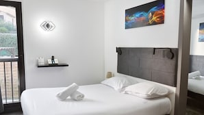 Habitación de hotel con cama, cabecero, estante en la pared con artículos de tocador y un cuadro sobre la cama.